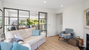 A modern living room with a large sectional sofa, a striped armchair, and a dining area visible through glass doors.