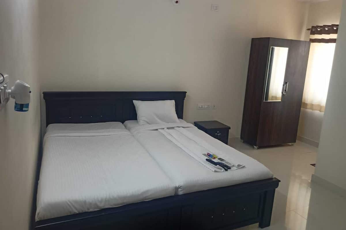 A double bed with white linens, a dark headboard, a bedside table, a wardrobe, and a mirror.