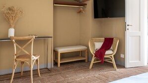 A room with a wooden chair, a bench, a television mounted on the wall, and a door.