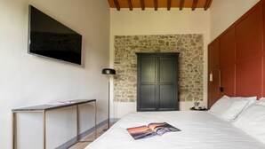 Un dormitorio con una cama, un escritorio, un televisor, una pared de piedra y una puerta de madera.