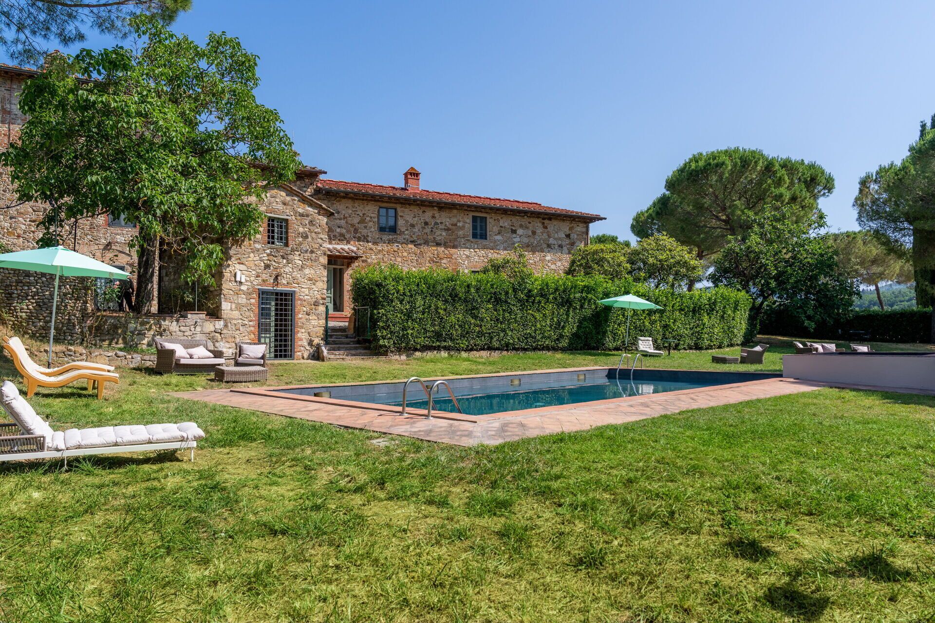 A stone house with a swimming pool, outdoor seating, and a well-maintained lawn.