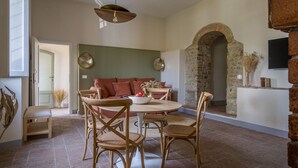 A dining area with a round table, wooden chairs, a sofa, and a stone wall with an archway.