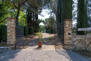 Une entrée fermée par un portail, avec des piliers en pierre, un chemin de gravier et une enseigne indiquant la réception.