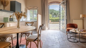 A cozy kitchen with a dining area, a vintage microwave, and a view of the garden through an open door.
