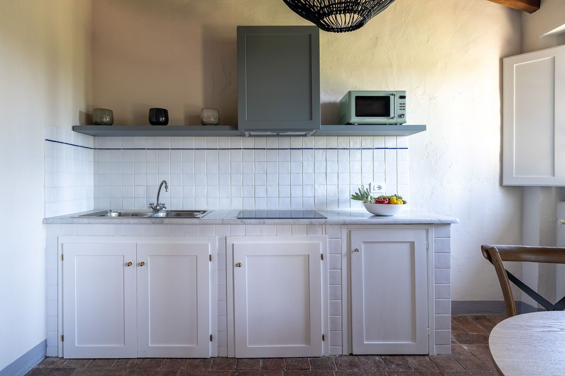 A compact kitchen with white cabinets, a stainless steel sink, a microwave, and a bowl of fruit on the countertop.