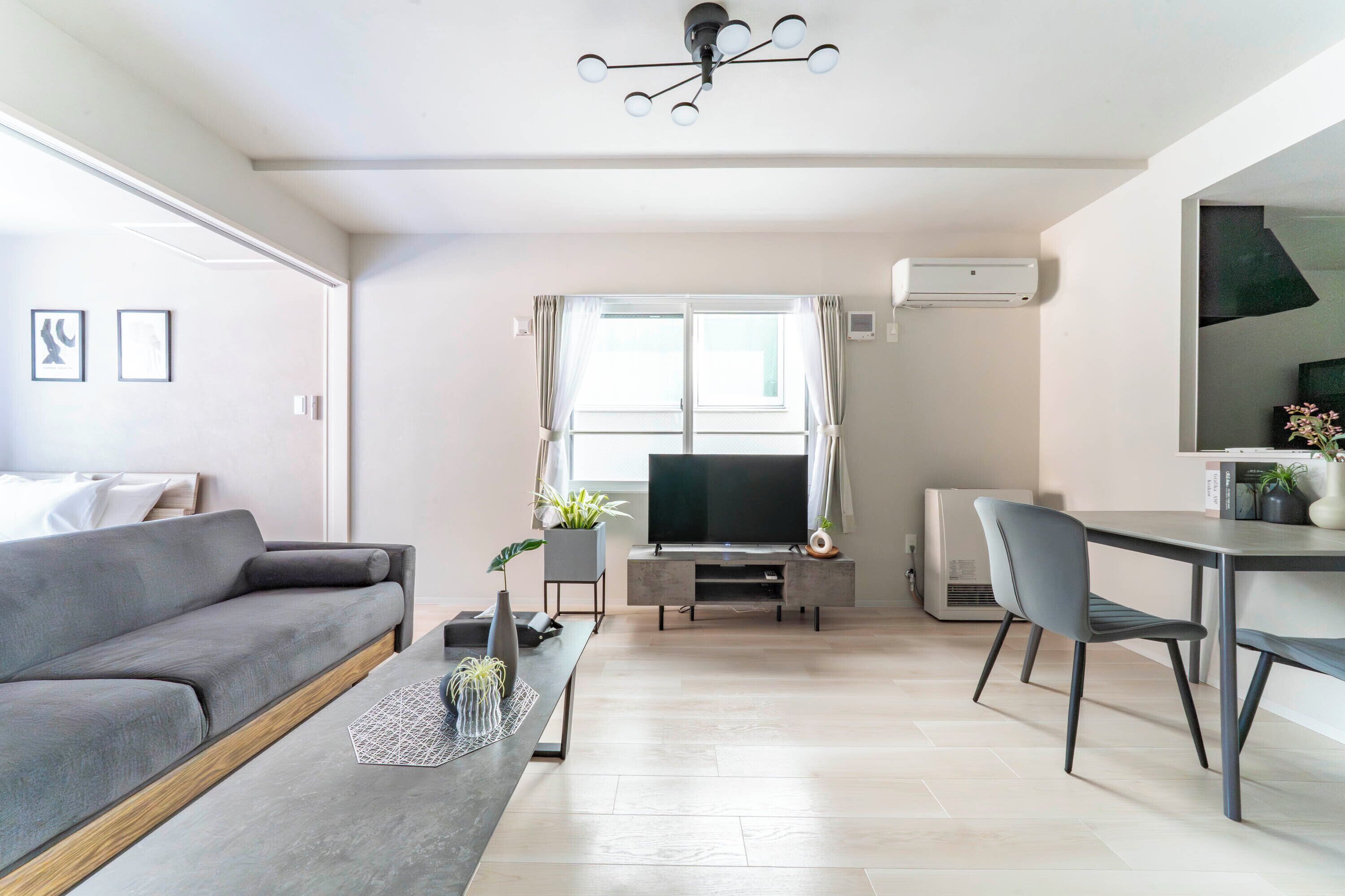 A modern living room with a grey sofa, a dining table, and a TV.