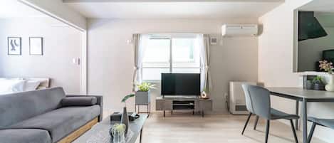 A modern living room with a grey sofa, a dining table, and a TV.