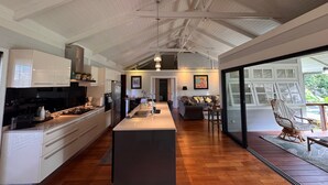A spacious kitchen with a central island, wooden flooring, and a large dining area with a view of the outdoors. - Charming 2-bedroom house in welcoming Papeete with WiFi, AC (Papeete)