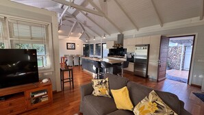 A spacious living area with a grey sofa, a flat-screen TV, wooden flooring, and a kitchen in the background. - Charming 2-bedroom house in welcoming Papeete with WiFi, AC (Papeete)