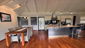 A modern kitchen with wooden flooring, a dining area with a wooden table and chairs, and a large island with bar stools. - Charming 2-bedroom house in welcoming Papeete with WiFi, AC (Papeete)