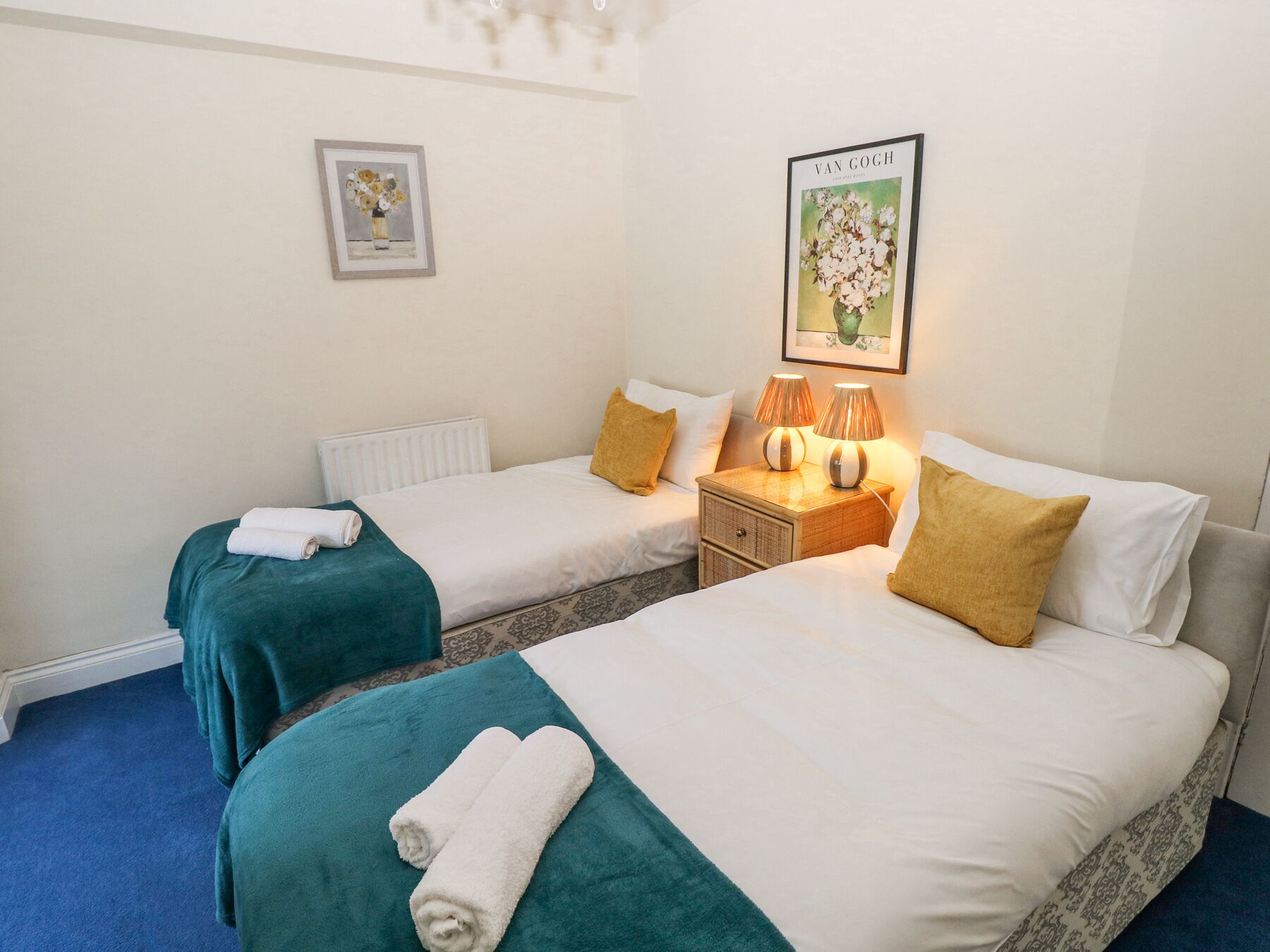 A hotel room with two single beds, a nightstand with lamps, and a framed picture on the wall.
