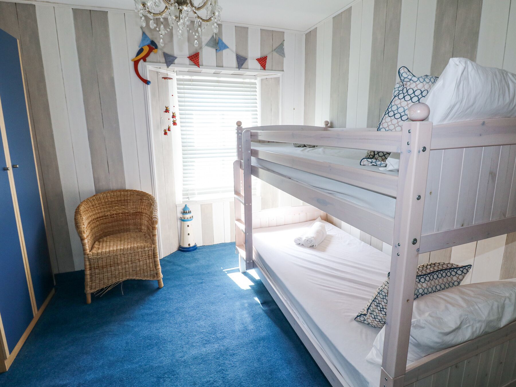 A bunk bed room with a wicker chair, a lighthouse decoration, and a chandelier.