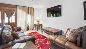 A living room with leather sofas, a red patterned rug, a wooden coffee table, and a TV mounted on the wall. - Calm & Spacious Retreat • Family-Ready Escape (Plant City)