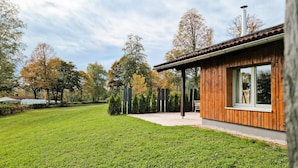 A modern house with a wooden exterior, a covered porch, and a well-maintained lawn. - Tiny Home 'Ferdl' with Mountain View, Private Garden and Wi-Fi (Untergriesbach)