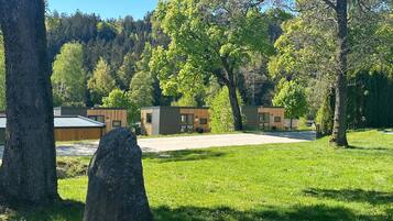 Ein Campingplatz mit modernen Holzhütten, einem gepflasterten Weg und einer Rasenfläche mit Bäumen.