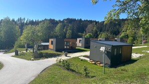 A modern outdoor area with a paved path, wooden benches, and a small building with a dark roof. - Tiny Home 'Ferdl' with Mountain View, Private Garden and Wi-Fi (Untergriesbach)