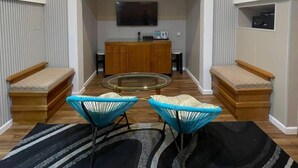 A modern living room with a high ceiling, a flat-screen TV mounted on the wall, a wooden cabinet, and two blue chairs with cushions. - Suite Sharilla (Pulau Perhentian Kecil)