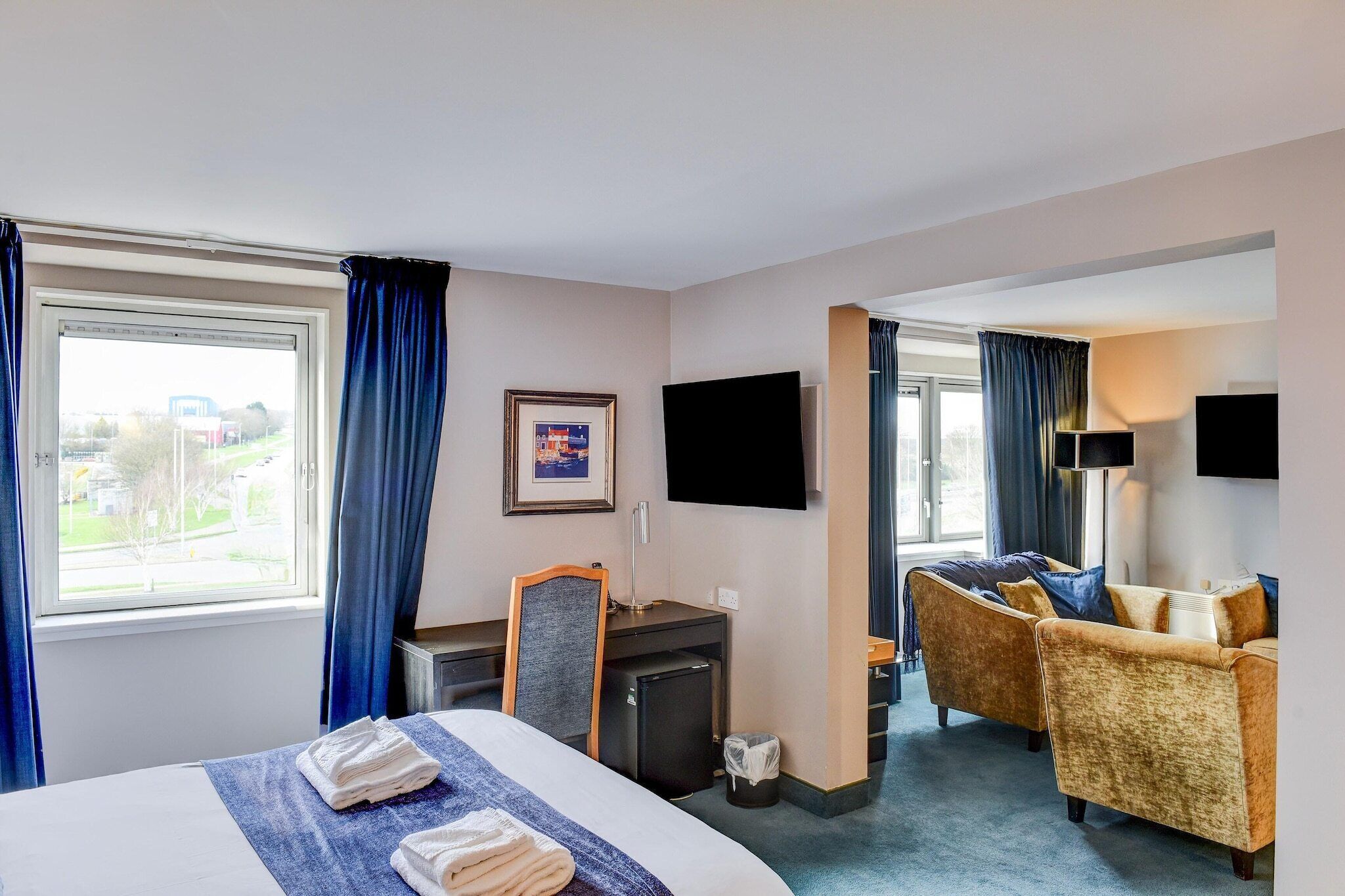 A hotel room with a bed, desk, chair, TV, and a view of the outdoors.