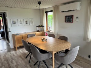 Un comedor con mesa de madera y sillas grises, una lámpara colgante, una ventana con cortinas y cuadros en la pared.