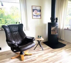 A room with a leather chair, a small wooden table, a black wood-burning stove, and a poster on the wall.