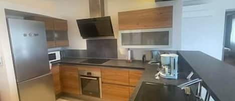 A modern kitchen with stainless steel appliances, wooden cabinets, and a black countertop.