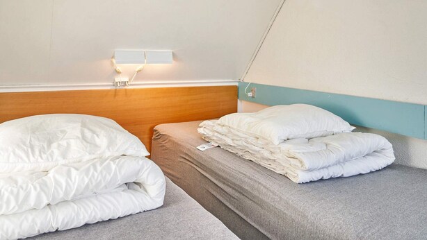 Habitación de hotel con dos camas individuales, cabecero de madera, luz de pared y un diseño sencillo y limpio.