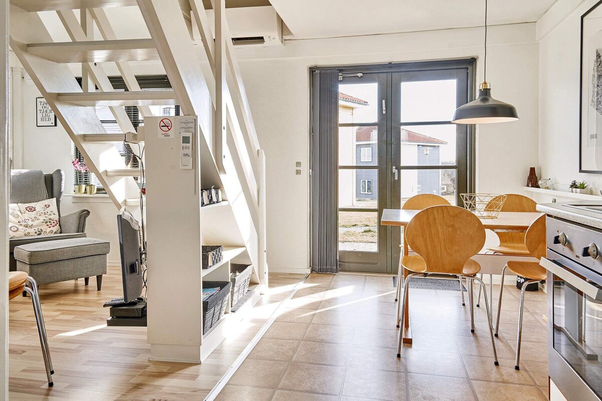 Una cocina moderna con comedor, sillas de madera y una escalera que sube a un altillo.