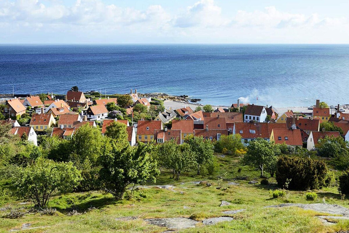 Ein Küstendorf mit traditionellen Häusern mit roten Dächern, einem grasbewachsen Vordergrund und Blick aufs Meer.