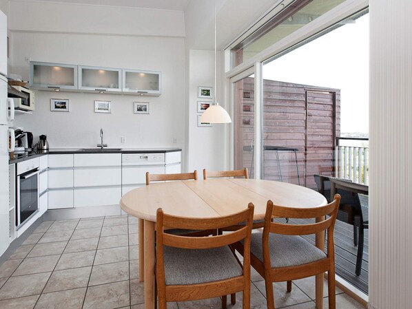 Une cuisine moderne avec des meubles blancs, une table à manger avec des chaises et un balcon offrant une vue agréable.