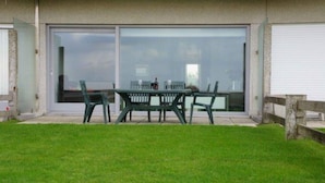 Une terrasse avec une table et des chaises, une porte-fenêtre coulissante et une pelouse.