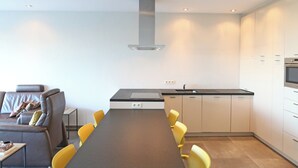 Une cuisine moderne avec un grand îlot central, des chaises jaunes et un canapé gris.