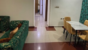 Un'ampia zona giorno con un divano verde, un tavolo da pranzo con sedie e una cucina visibile attraverso un arco.