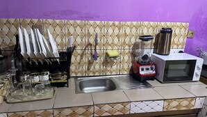 A kitchen with a sink, a microwave, and a blender. There are utensils hanging on a rack, and a shelf with jars and glasses. - Appartement Meublé Moderne - Centre-ville Yaoundé (Air Conditioning, Wi-Fi, Security) (Yaoundé)