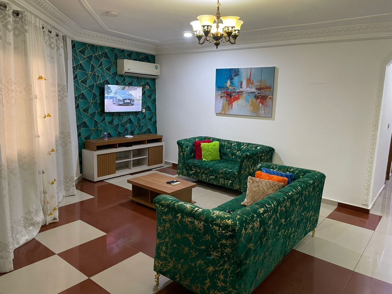 A living room with two green sofas, a wooden coffee table, a TV on the wall, and a painting.