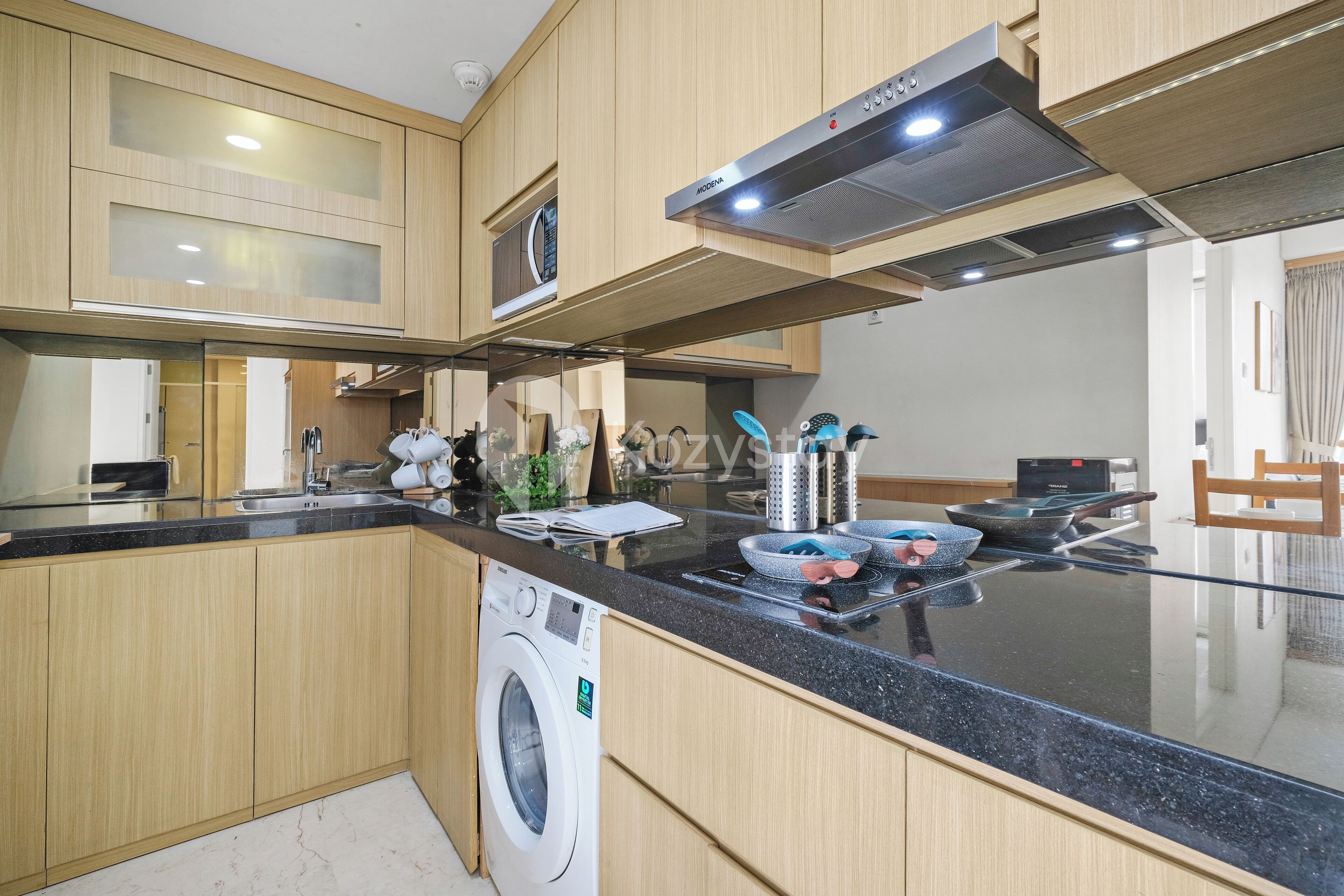 A modern kitchen with wooden cabinets, a built-in washing machine, a stainless steel range hood, and a black countertop.