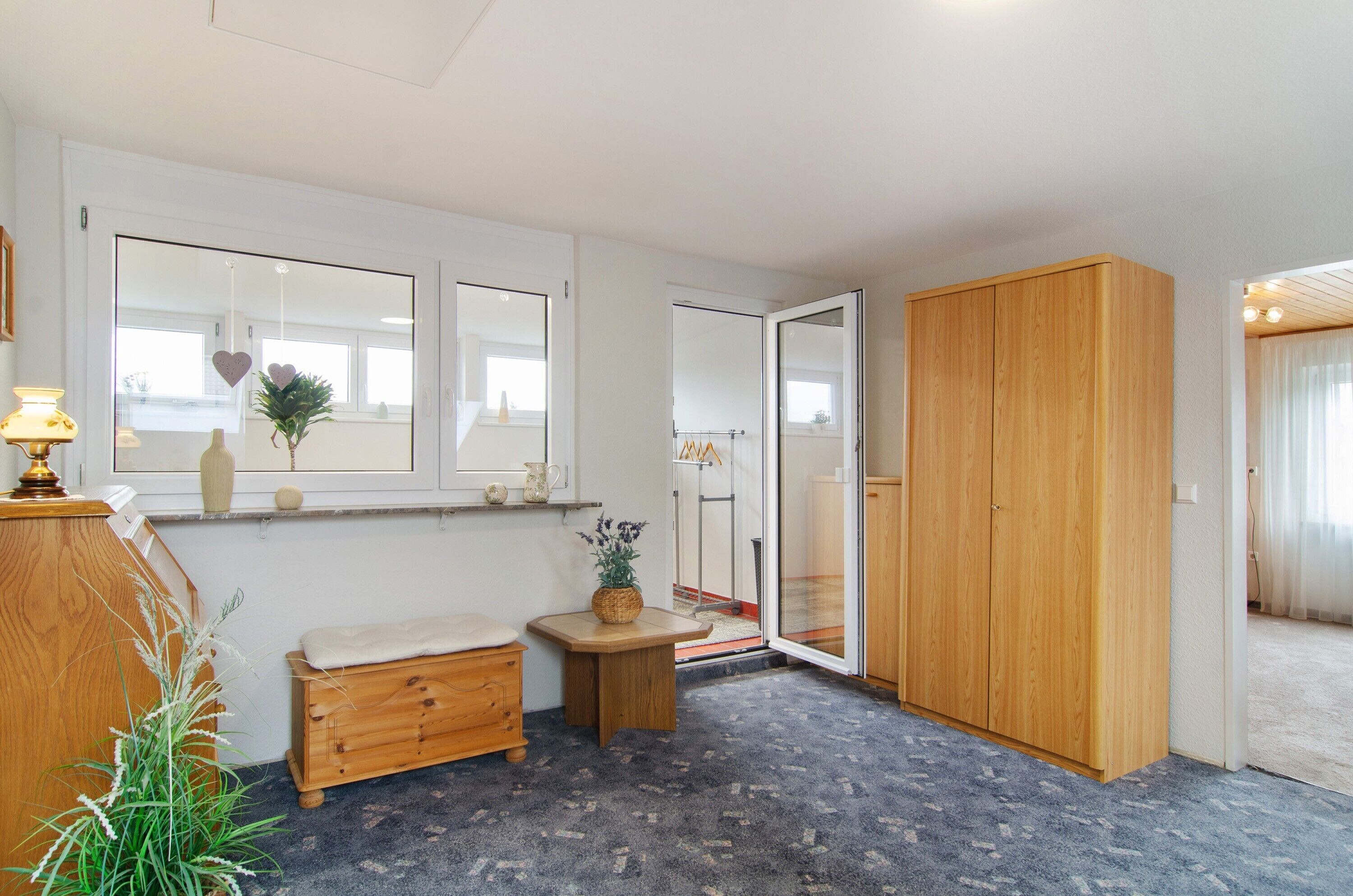 Ein Zimmer mit einer hölzernen Sitzbank, einem kleinen Tisch mit einer Pflanze, einem Kleiderschrank und einem Fenster mit Blick.