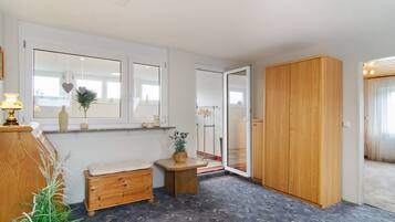 Ein Zimmer mit einer hölzernen Sitzbank, einem kleinen Tisch mit einer Pflanze, einem Kleiderschrank und einem Fenster mit Blick.