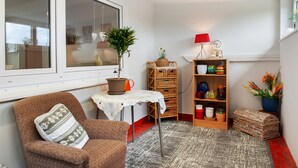 Una habitación acogedora con una silla, una mesita con una planta, una estantería y una ventana.