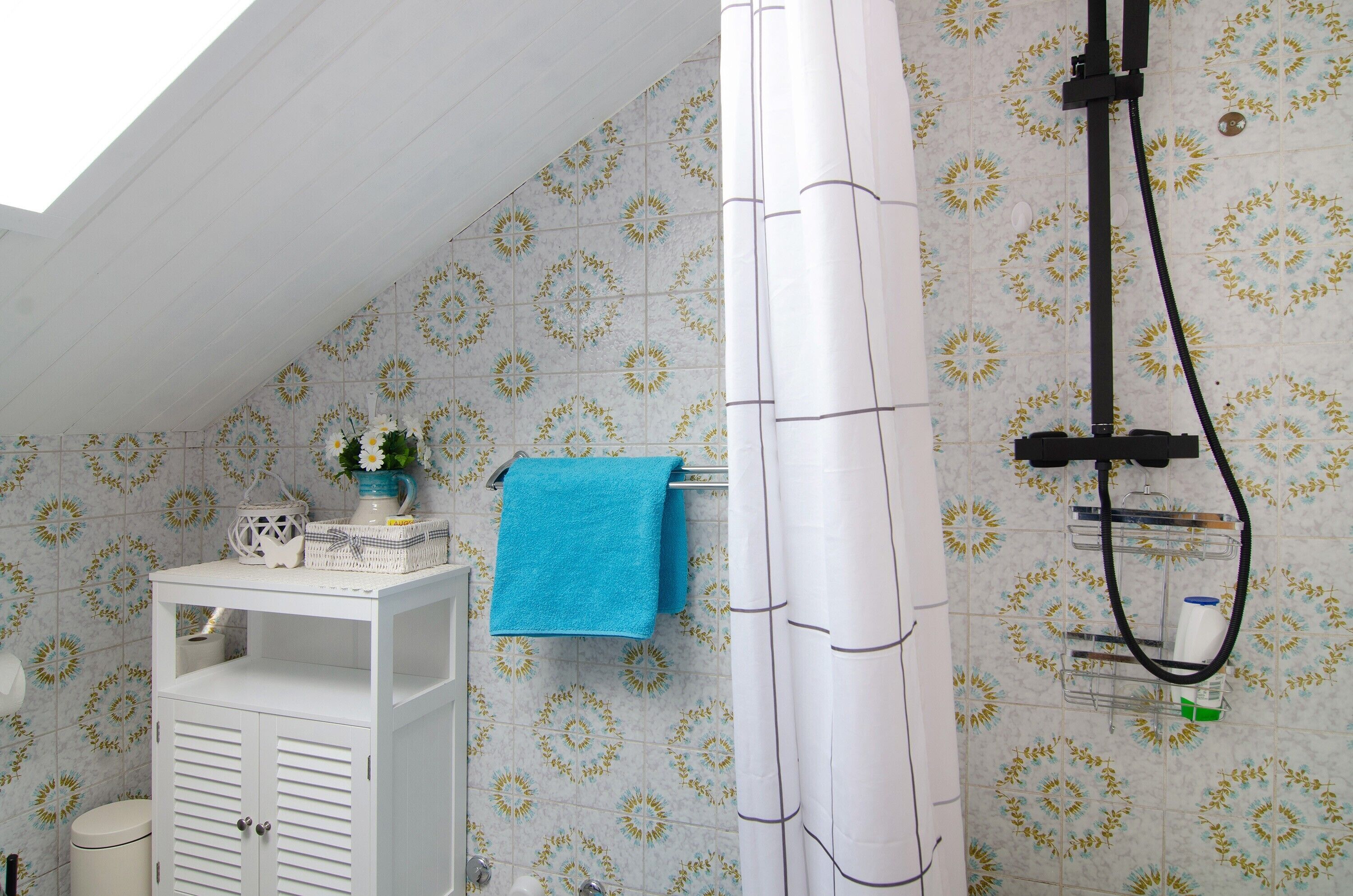 Ein Badezimmer mit Dusche, Handtuchhalter, einem kleinen Tisch mit einer Vase und einer Toilette.