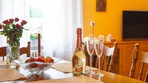 Una mesa de comedor con una botella de vino, copas, un frutero y un jarrón con flores.
