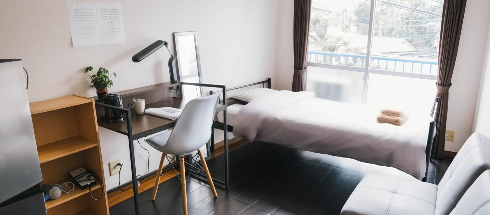 Habitación de hotel pequeña con escritorio, silla, dos camas, una planta y ventana con cortinas.