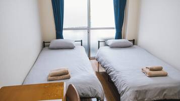 Una habitación con dos camas individuales, una mesa de madera y un ventanal con cortinas.