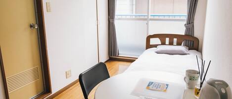 A hotel room with a bed, a table with a remote control, a cup, and a kettle.