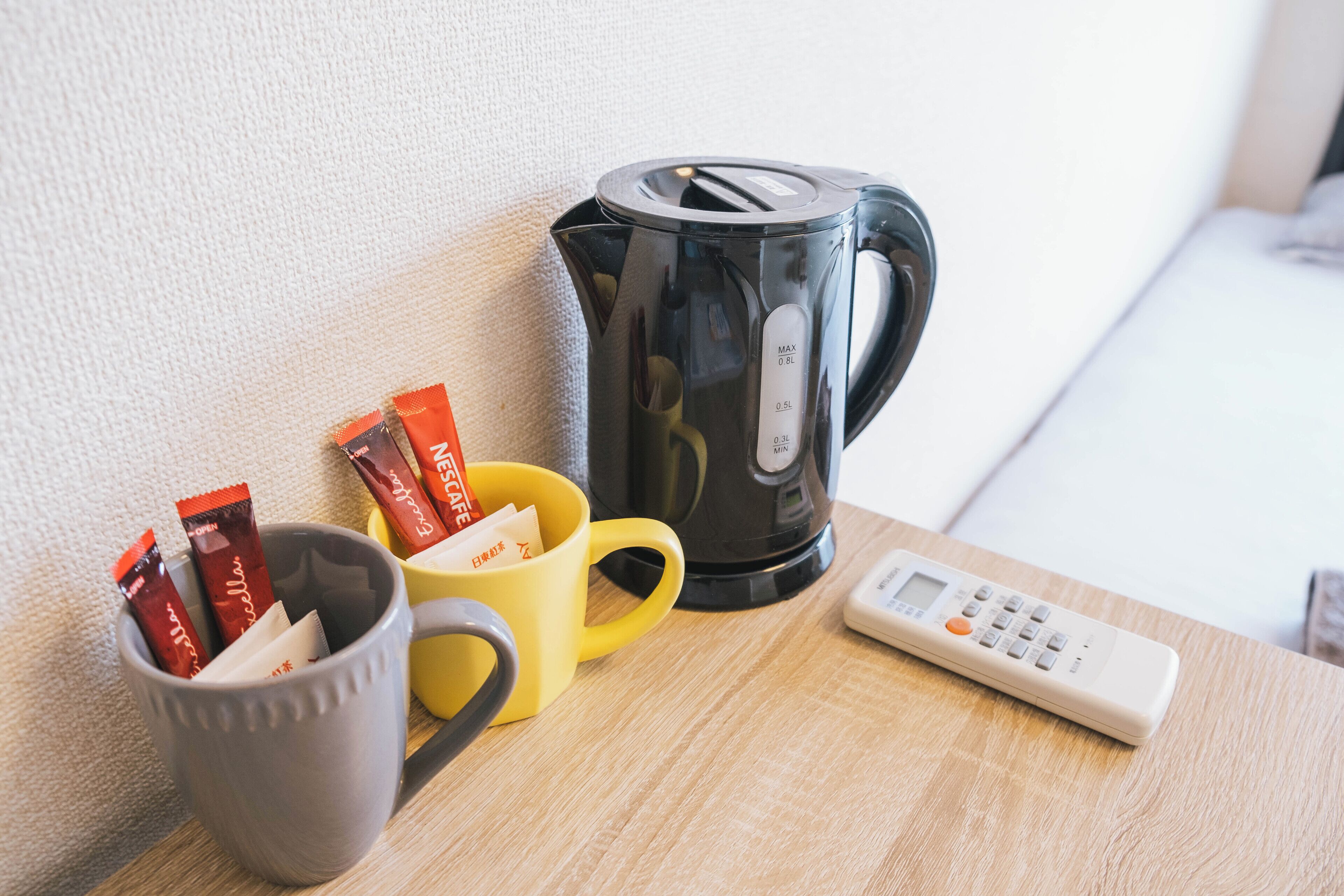 A coffee maker, two mugs, and a remote control on a wooden table.