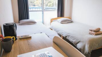 A hotel room with two single beds, a wooden table with a coffee maker, a remote control, and a book on the table.
