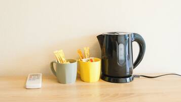 Une table en bois, sur laquelle se trouvent une bouilloire électrique noire, une tasse grise et une tasse jaune contenant des sachets.