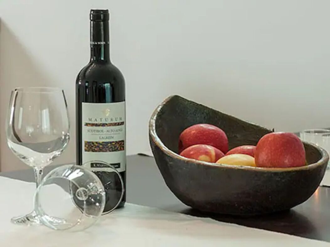 Una botella de vino, una copa de vino y un bol con frutas sobre una mesa.