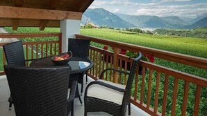 Un balcone con mobili in vimini e un tavolo, affacciato su un paesaggio verde e montagne.
