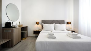 Une chambre d’hôtel moderne avec un lit soigneusement fait, deux tables de chevet avec des lampes, un grand miroir rond et un bureau en bois avec une machine à café.