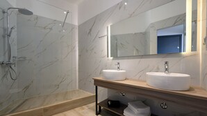 Une salle de bain moderne dotée d’une douche à parois de verre, de deux lavabos et d’un grand miroir.